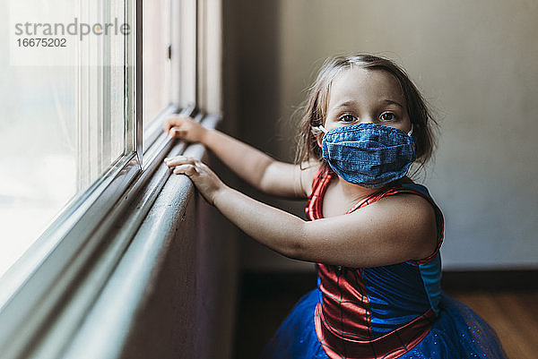 Mädchen im Vorschulalter in Halloween-Kostüm und Gesichtsmaske am Fenster