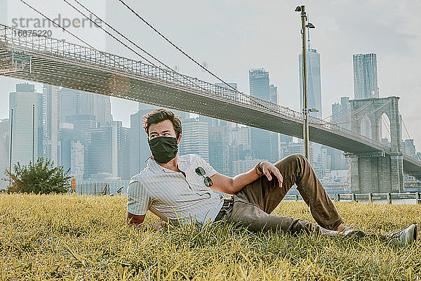 Junger Mann sitzt im Park und trägt eine Gesichtsmaske.