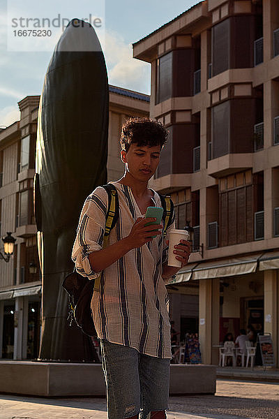 Ein junger Mann mit Afrohaar geht bei Sonnenuntergang spazieren und benutzt dabei sein Handy