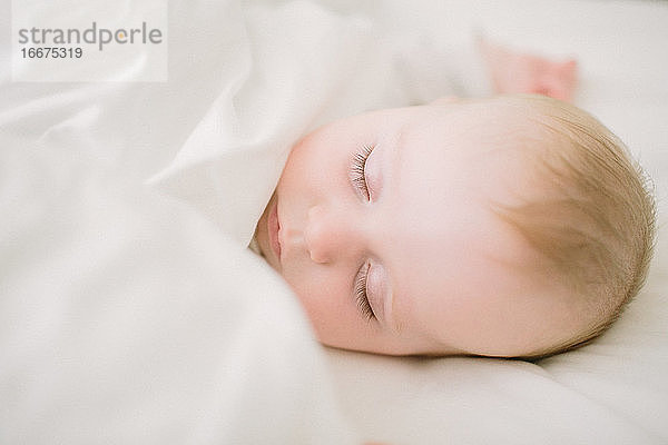 Friedlich und ätherisch schlafendes Baby umgeben von einer weißen Decke