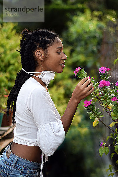 Junge Frau nimmt Gesichtsmaske ab  um an den Blumen zu riechen