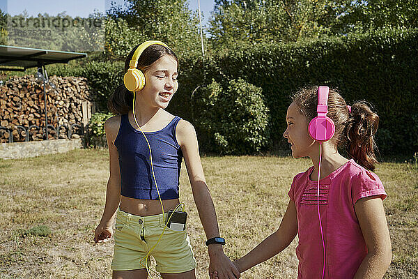 Kleine Mädchen  die sich umarmen und mit gelben und rosa Kopfhörern im Garten Musik hören. Sommer Konzept