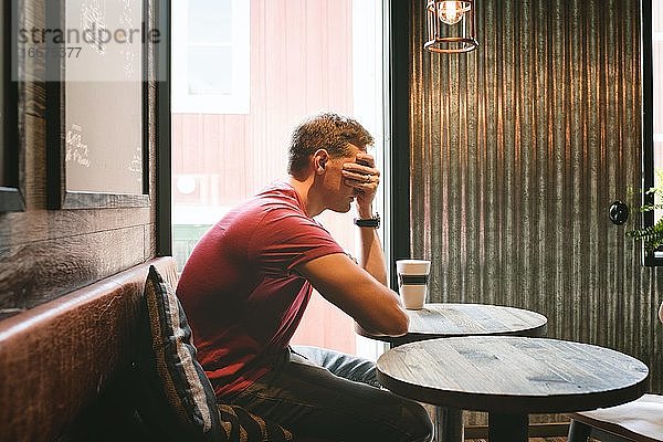 Mann saß in einem Café und bedeckte sein Gesicht  während er sich gestresst fühlte