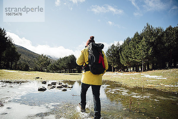 Junger Mann mit gelber Jacke und Rucksack neben einem Teich in den Bergen