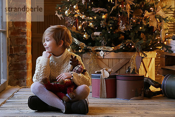 Bild eines Kindes in der Nähe eines Weihnachtsbaums in warmen Farben.