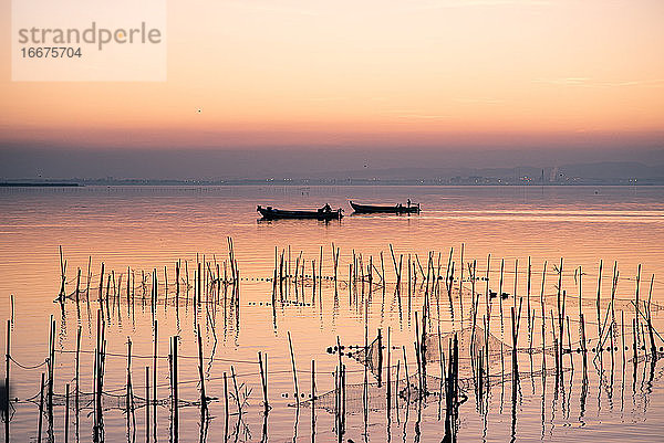 Zwei Boote und Fischernetze bei Sonnenuntergang in der Albufera im Gegenlicht