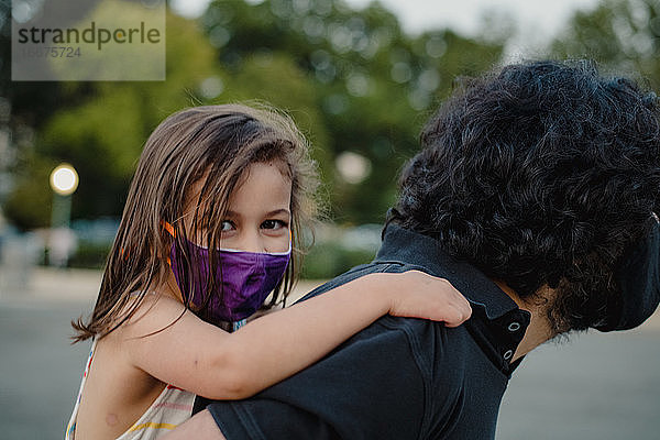 Kleines Mädchen reitet auf Papas Rücken und trägt Gesichtsmaske