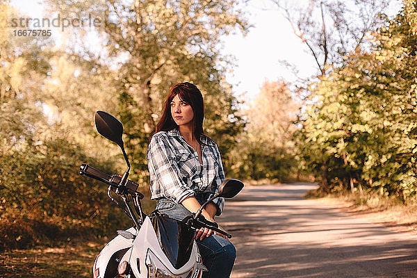 Nachdenkliche junge Frau  die auf einem Motorrad sitzend wegschaut