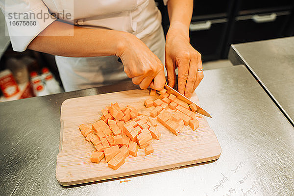 Hände einer Köchin beim Schneiden von Kürbis an der Küchentheke eines Restaurants