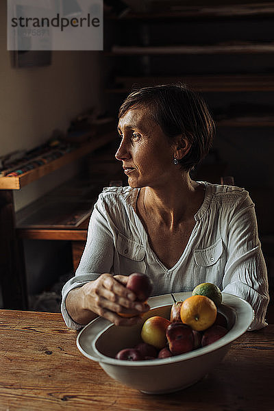 Frau mittleren Alters sitzt am Tisch mit einer Schale mit Früchten