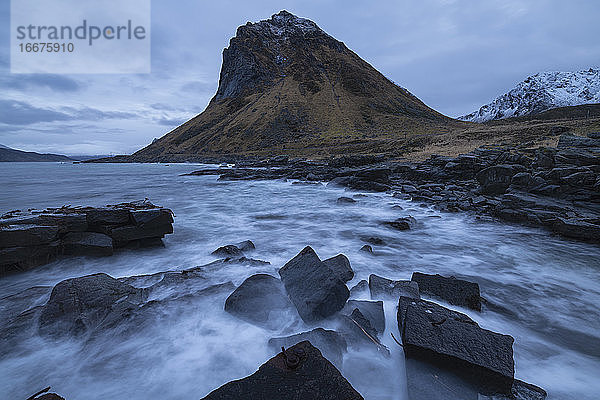 Der Berggipfel Slettind erhebt sich über dem Wellenbrecher in Myrland  Flakstadøy  Lofoten  Norwegen