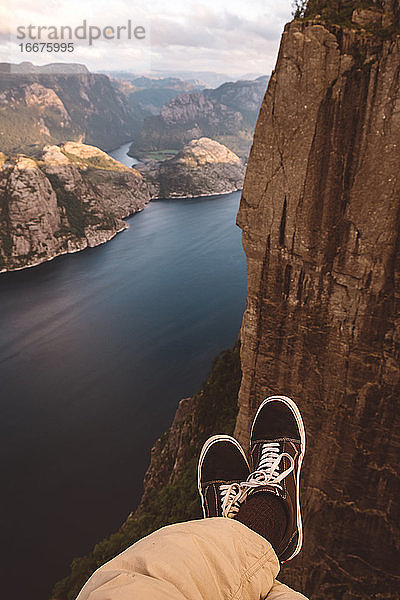 Person im Schneidersitz am Rande einer Klippe mit Blick auf die Fjorde in Norwegen