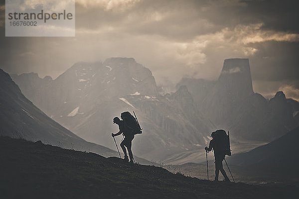 Silhouette von zwei Rucksacktouristen beim Wandern mit Blick auf schroffe Berge.