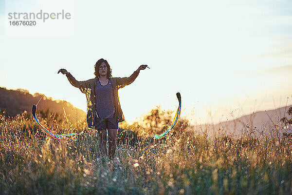 Eine Frau jongliert bei Sonnenuntergang. Sie ist auf einer schönen Wiese auf dem Land.