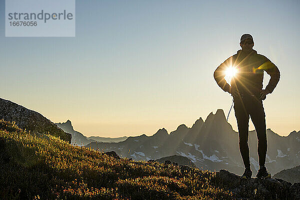 Die Sonne scheint durch den Arm eines silhouettierten Wanderers auf einem Bergkamm