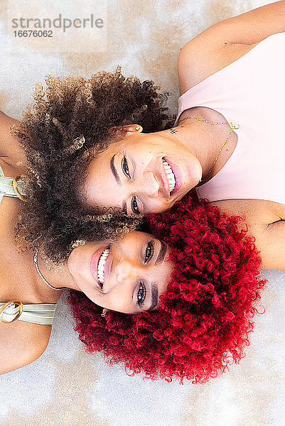 Zenithales Porträt zweier lateinamerikanischer Frauen mit Afro-Haar auf dem Boden.