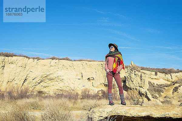 Schöne Frau mit Hut und Sonnenbrille steht in der Wüste und schaut in die Kamera