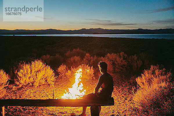 Junger Mann sitzt nachts am Lagerfeuer in der Nähe des Mono Lake in Kalifornien.