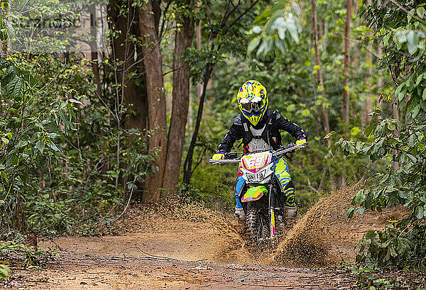 Frau fährt mit ihrem Geländemotorrad auf einem Waldweg in Pak Chong / Thailand