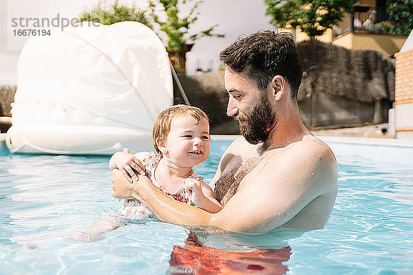 Mann in einem Hausschwimmbad mit einem kleinen Mädchen im Arm schwimmend
