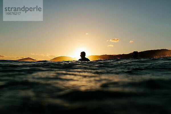 Surfer-Silhouette im Wasser sitzend bei Sonnenuntergang