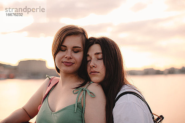 Porträt eines glücklichen lesbischen Paares  das bei Sonnenuntergang auf einer Brücke steht