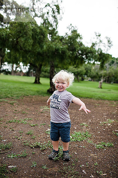 Zweijähriges Mädchen lächelt für die Kamera und steht im Park
