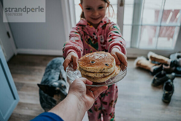 Porträt einer Person  die einem kleinen Mädchen im Pyjama Pfannkuchen reicht