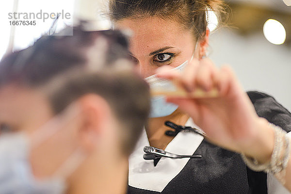 Friseurin bei der Arbeit mit Gesichtsmaske beim Styling eines jungen Mädchens