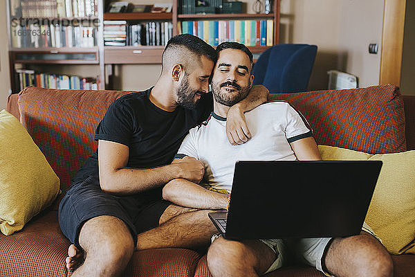 Romantisches schwules Paar mit Laptop auf dem Sofa
