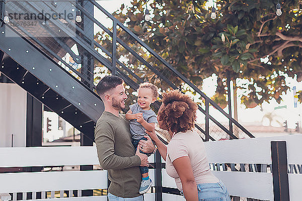 Der Vater hält den kleinen Jungen und die Mutter versucht  ihn zum Lachen zu bringen