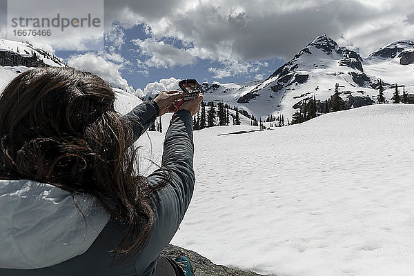 Unbekannte Reisende  die während einer Reise durch verschneite Berge an einem bewölkten Frühlingstag einen Kompass zur Navigation benutzt