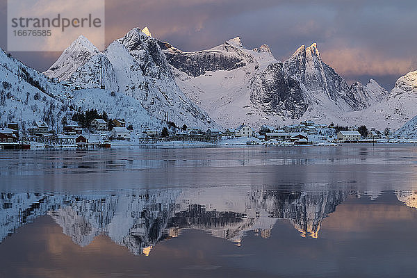 Die tiefstehende Januarsonne beleuchtet ferne Berggipfel über dem Reinefjord  Reine  Moskenesøy  Lofoten  Norwegen