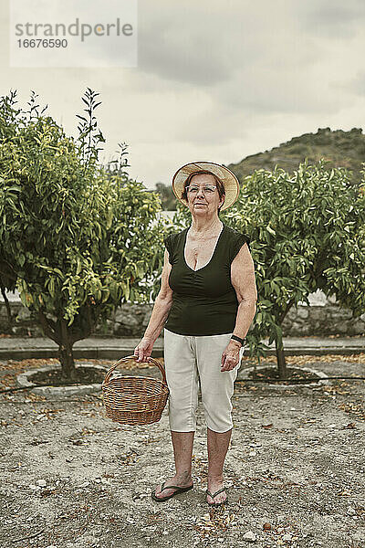 Porträt einer alten Dame mit Hut und Korb in ihrem kleinen Obstgarten
