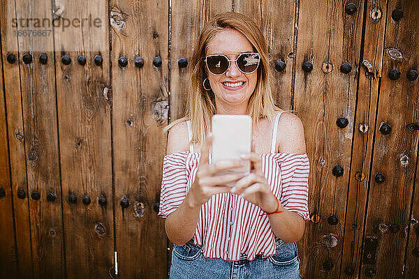 Blonde Frau lächelt und lacht  während sie auf ihr Mobiltelefon schaut