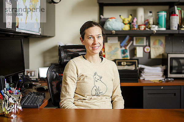 Eine lächelnde Professorin sitzt an ihrem Schreibtisch in einem Büro