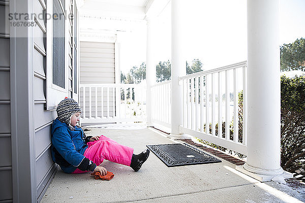 Wide View of Boy in Pink Snow Pants Sitting on Snowy Front Porch