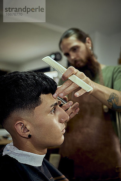 Ein Friseur arbeitet mit Kamm und Schere an einem jungen Mann