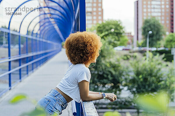 Frau mit Afro-Haar lehnt auf einer Brücke