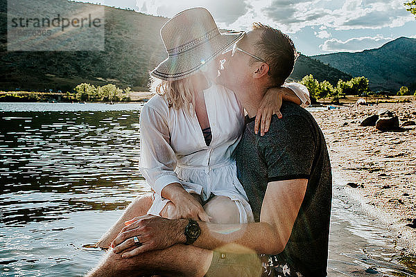 Mann und Frau sitzen zusammen und küssen sich am Seeufer
