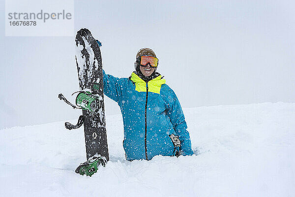 Glücklicher männlicher Wanderer mit Snowboard im Tiefschnee