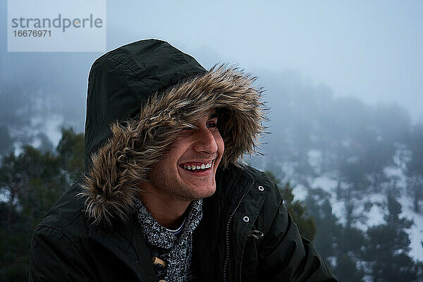 Lateinischer junger Mann lächelt in einem Mantel an einem verschneiten Tag