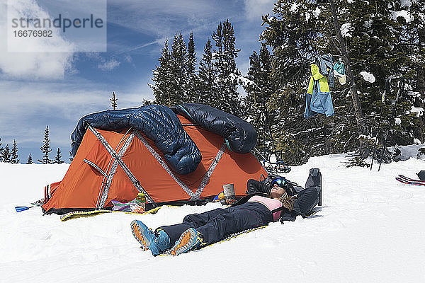 Junge Frau entspannt sich am Zelt auf einem schneebedeckten Berg