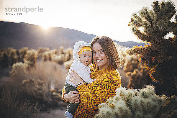 Eine Frau mit einem Baby steht in der Nähe eines Kaktus in der Wüste