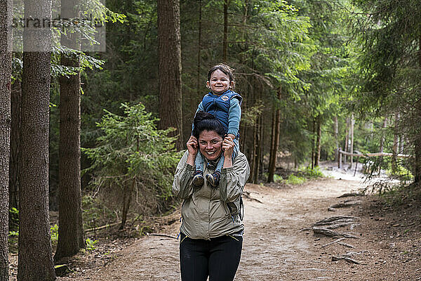 Porträt einer lächelnden Mutter  die ihren Sohn beim Wandern auf den Schultern trägt