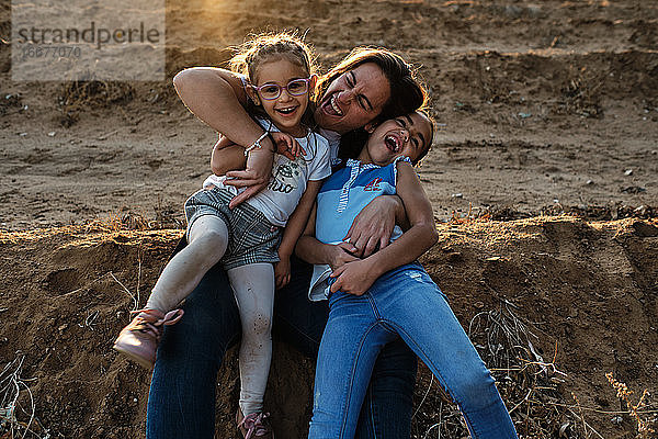 eine Mutter sitzt auf dem Spielfeld und spielt mit ihren Töchtern