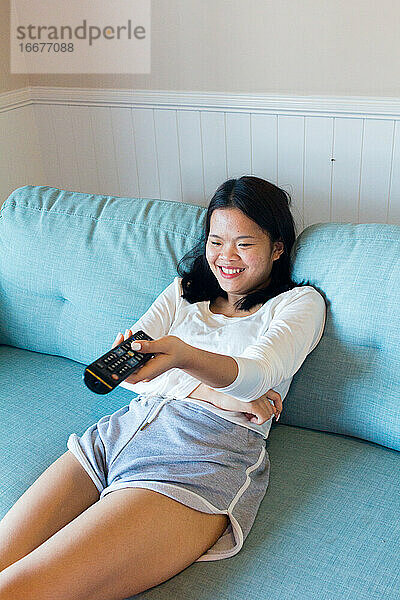 Asiatische Teenagerin sitzt lachend vor dem Fernseher