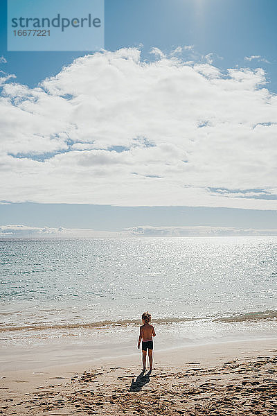 Junge  der an einem sonnigen Tag im Urlaub am Strand ins Wasser geht