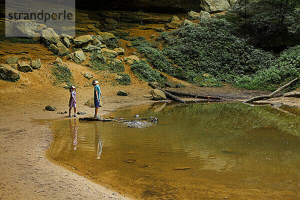 Zwei Kinder mit Masken stehen an einem Wasserbecken in einer Sandsteinschlucht