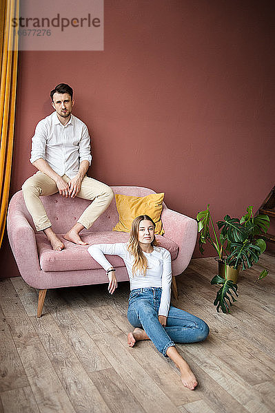 Ein Mann sitzt auf einem rosa Sofa mit dem Rücken zur Wand  eine Frau sitzt in der Nähe auf dem Boden.